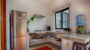 A compact kitchen with a stainless steel refrigerator, a gas stove, a sink, and a water dispenser.