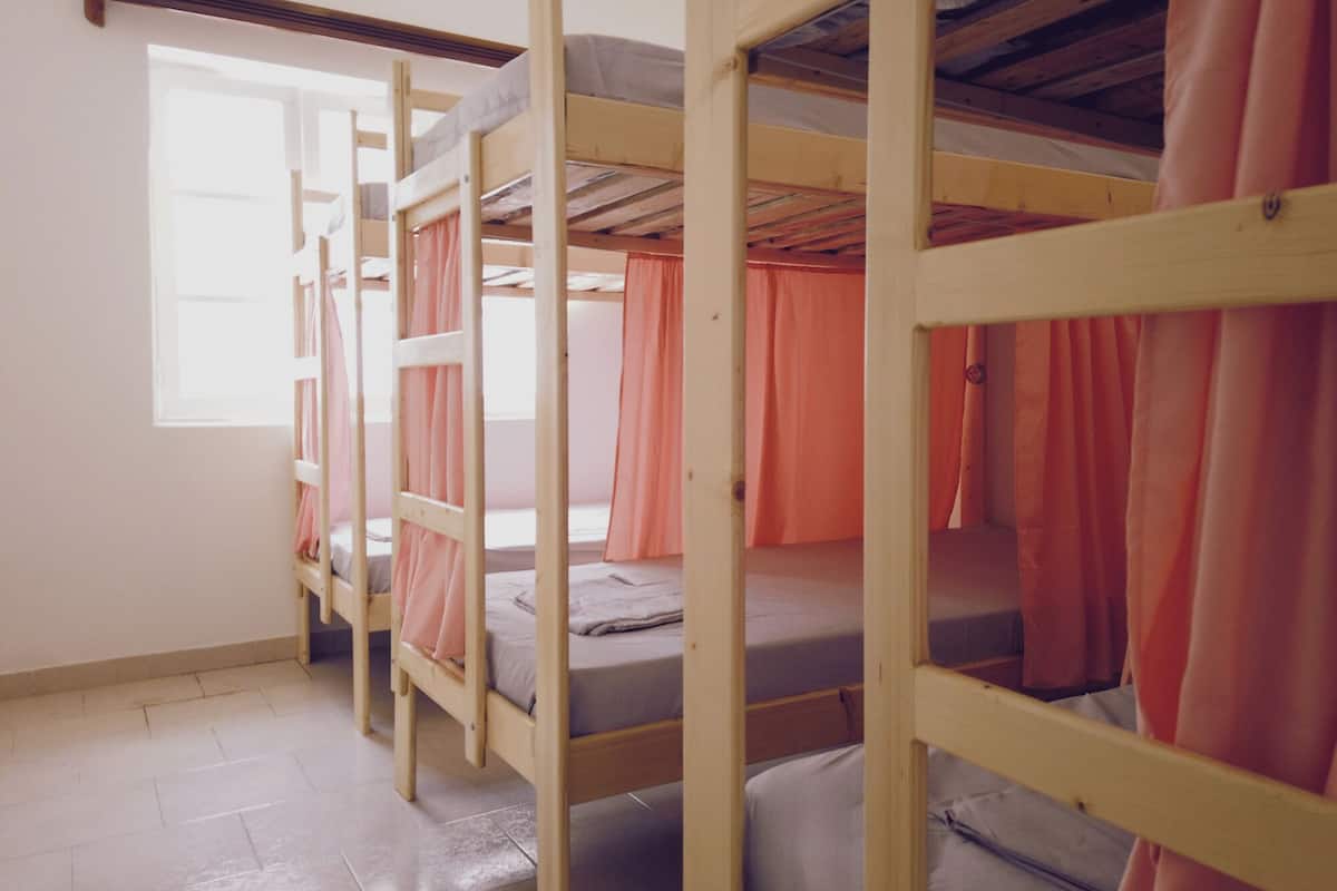 A dormitory room with bunk beds, a window, and orange curtains.