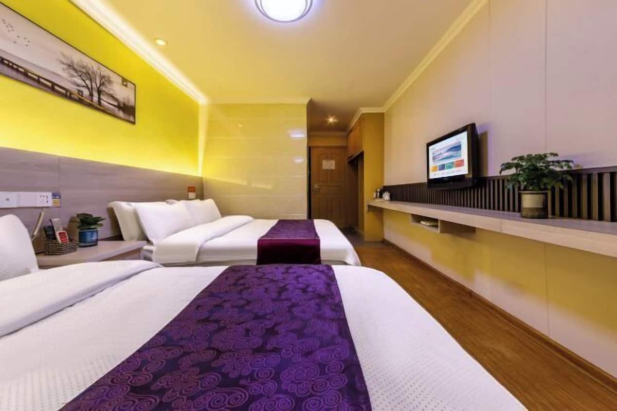 A hotel room with two beds, a TV, a plant, and a painting on the wall.