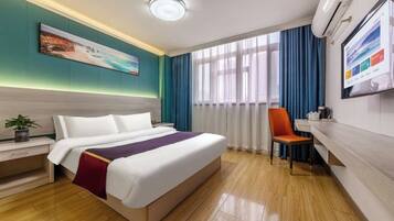 A hotel room with a bed, a desk, a chair, a window with curtains, and a wall-mounted TV.