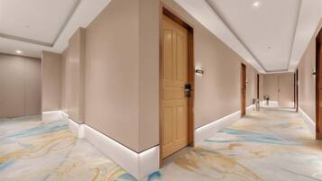 A hotel corridor with a wooden door, a marble-patterned floor, and a sign indicating the direction to the lobby.