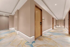 A hotel corridor with a wooden door, a marble-patterned floor, and a sign indicating the direction to the lobby. - Changsheng Hotel (Nanjing)