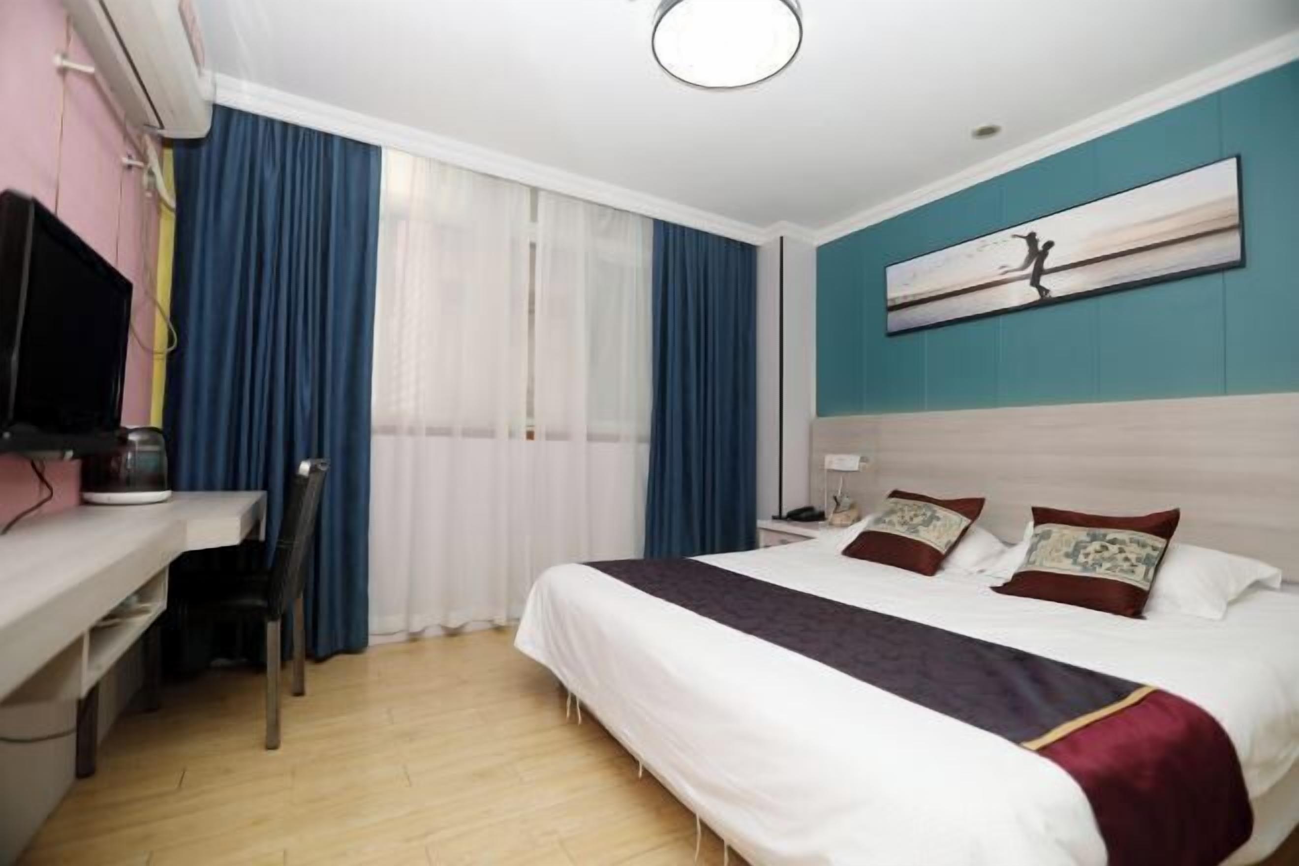 A hotel room with a bed, a desk, a chair, a TV, and a painting on the wall.