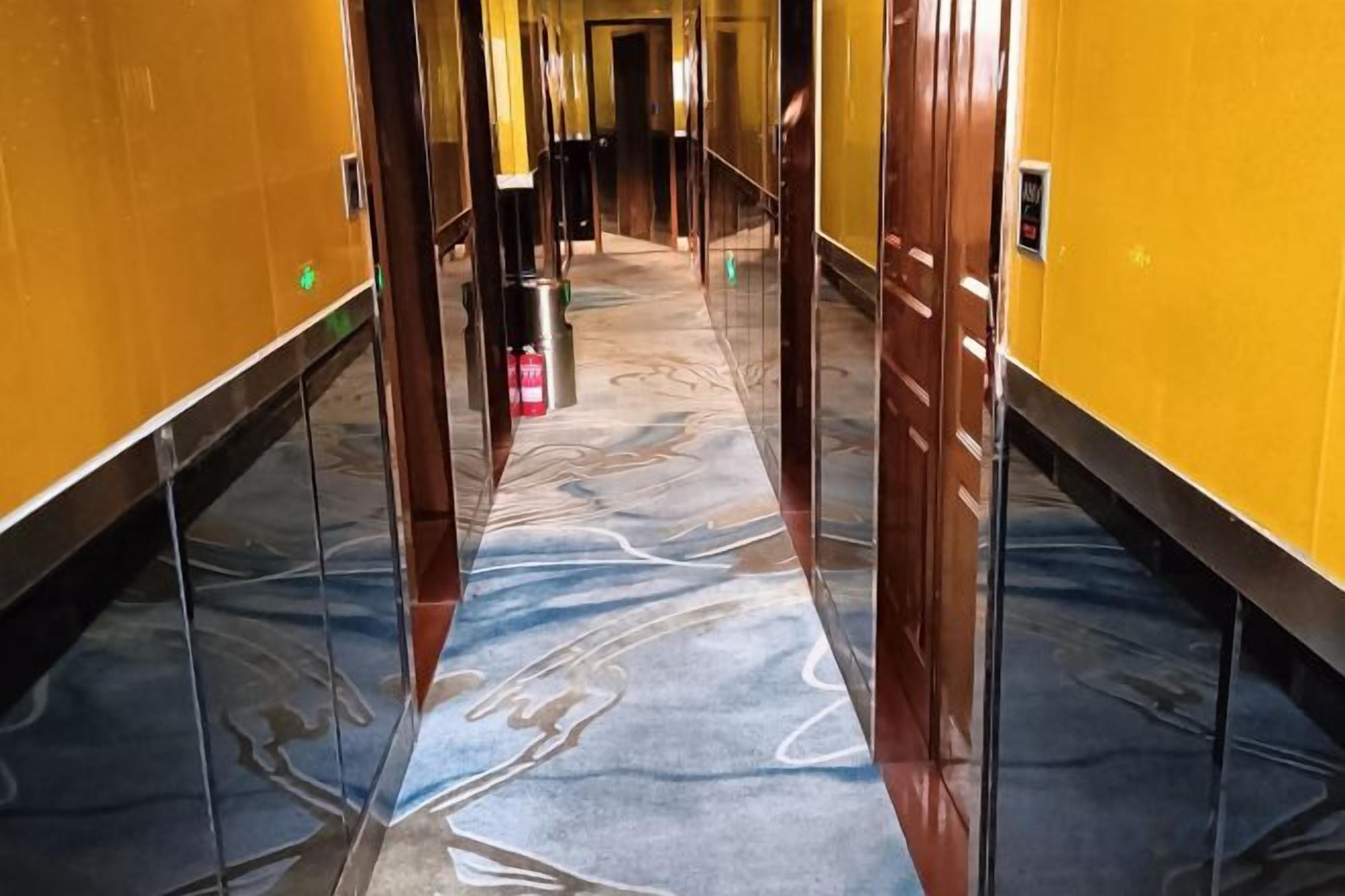 A hallway with a marble floor, yellow walls, and a door at the end.