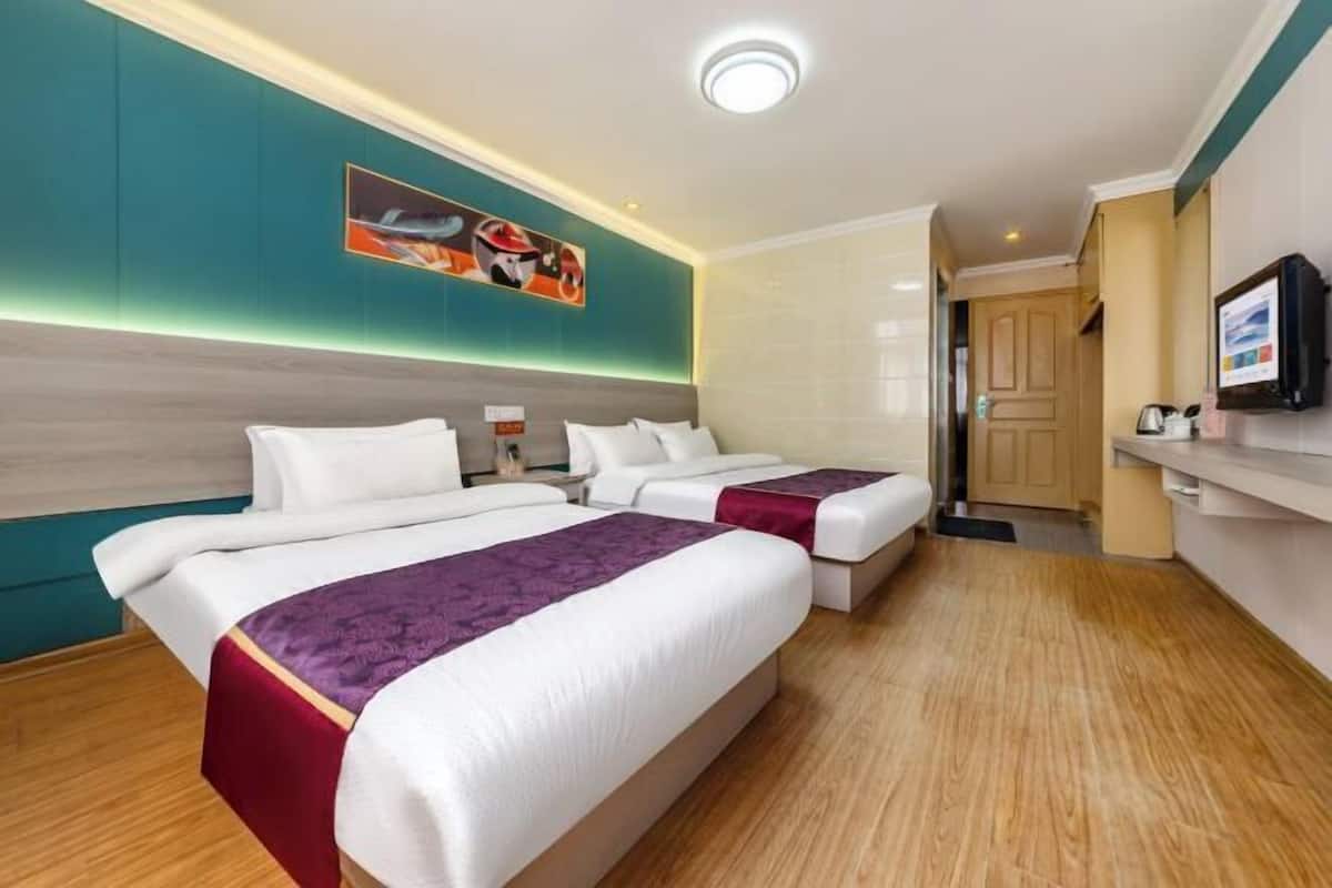 A hotel room with two beds, a TV, a painting on the wall, and a wooden floor.