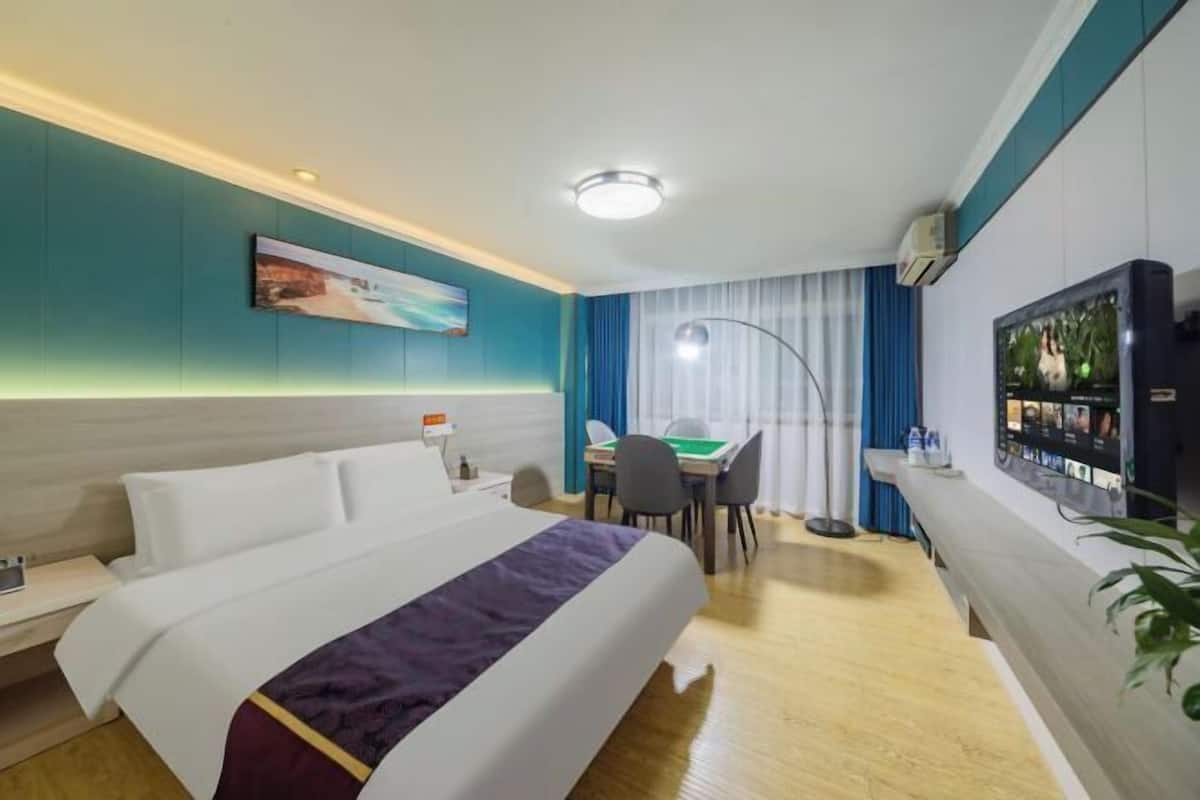 A hotel room with a bed, desk, chair, television, and a painting on the wall.