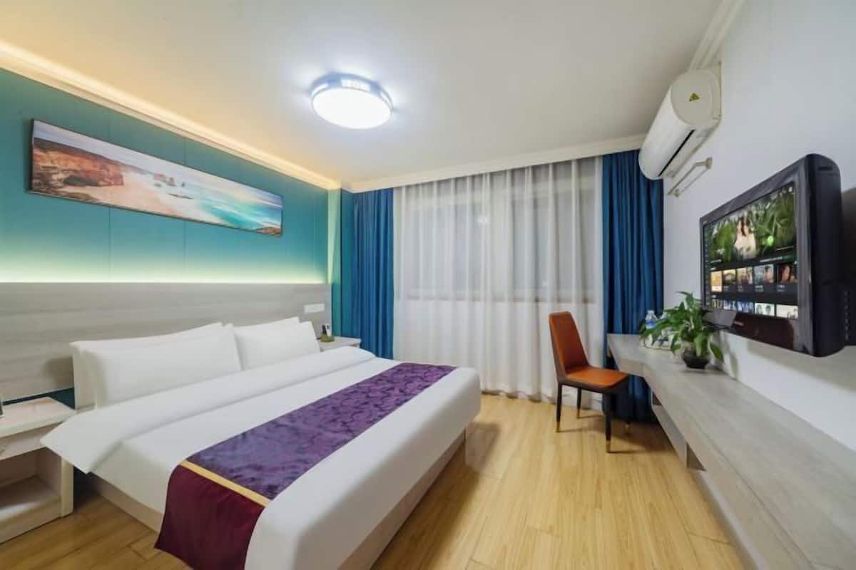 A hotel room with a bed, a desk, a chair, a TV, and a painting on the wall.