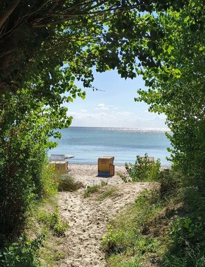 A beach view with a clear sky, a sandy path leading to the water, and two wooden benches.