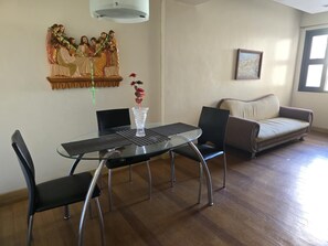 A dining area with a glass table, black chairs, a vase with flowers, a religious statue, a sofa, and a framed picture on the wall. - Cozy Apartment Oasis in San Dionisio (Parañaque)