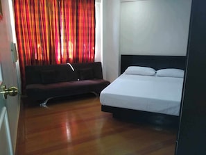A room with a bed, a sofa, and a window with curtains. - Cozy Apartment Oasis in San Dionisio (Parañaque)