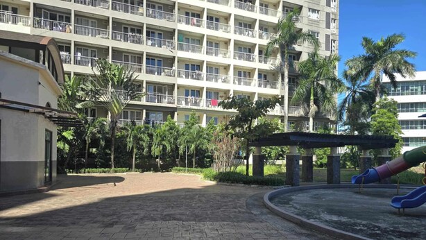 A courtyard with a playground, palm trees, and a multi-story building with balconies. - Cozy Apartment Oasis in San Dionisio (Parañaque)