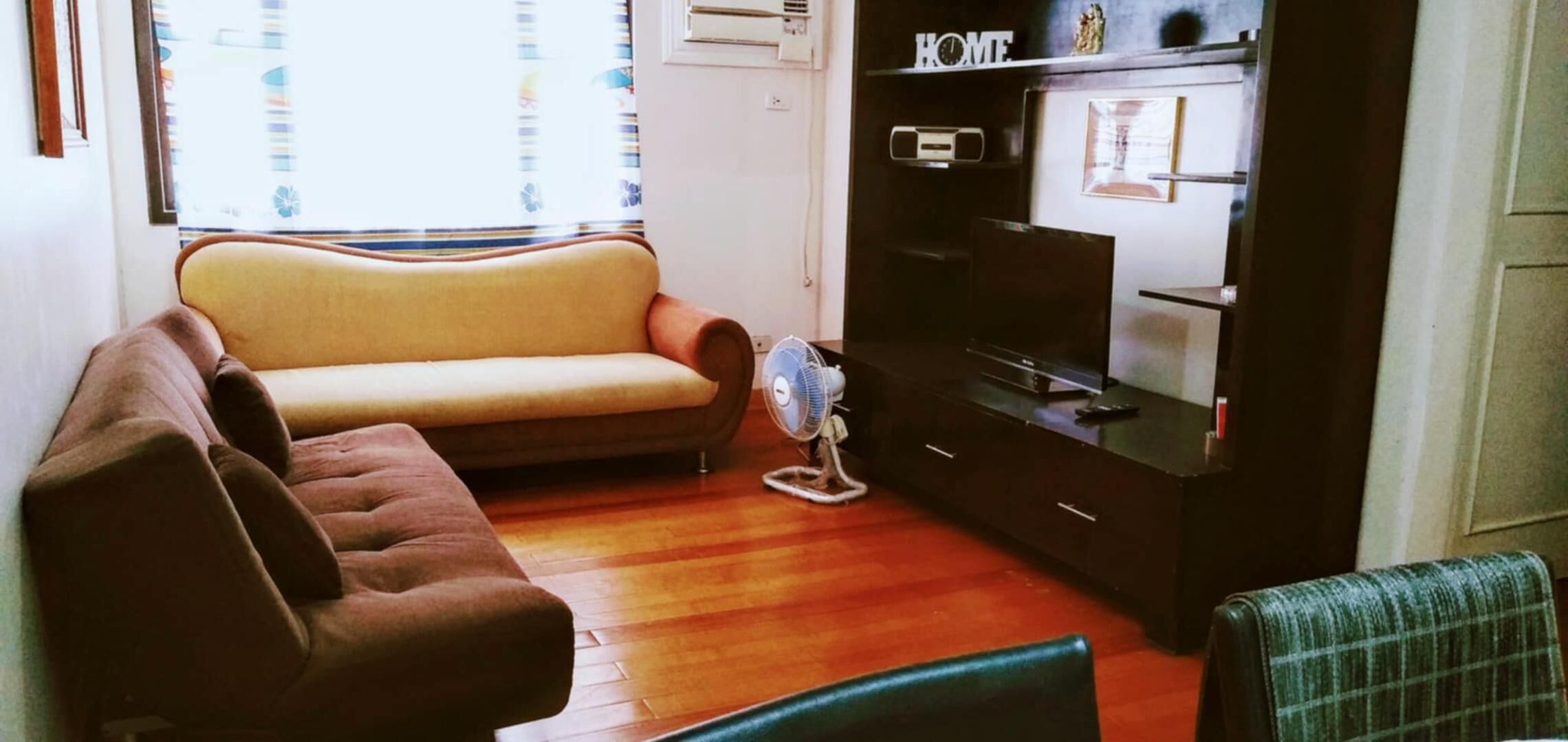 A living room with a sofa, a chair, a TV stand, and a fan.