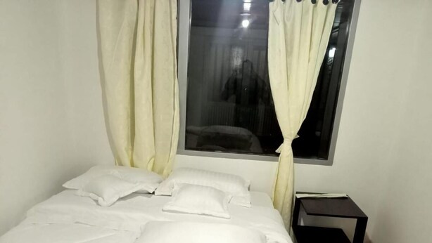 A bedroom with a bed, white curtains, a window, and a small table. - Hospedaje Cristiano Almagor (Bogotá)