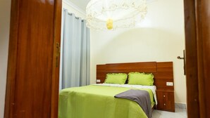 A bedroom with a wooden headboard, green bedding, a bedside table, and a chandelier.