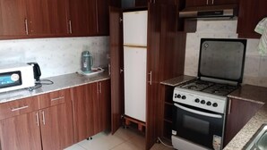 A compact kitchen with wooden cabinets, a white refrigerator, a gas stove, and a microwave.