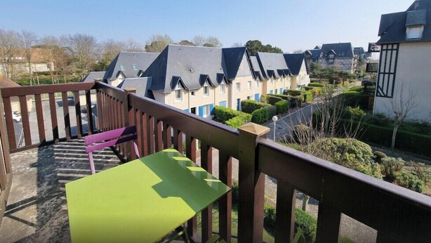 Ein Balkon mit einem grünen Tisch und einer violetten Bank, mit Blick auf eine Reihung von Häusern mit Giebeln und einem gepflegten Garten.