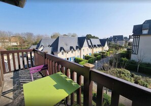 Ein Balkon mit einem grünen Tisch und einer violetten Bank, mit Blick auf eine Reihung von Häusern mit Giebeln und einem gepflegten Garten.
