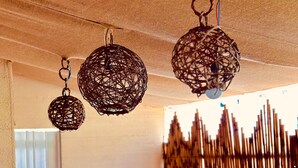 A dining area with round tables and chairs, hanging woven light fixtures, and a bamboo wall. - Pousada Golfinho (Fernando de Noronha)