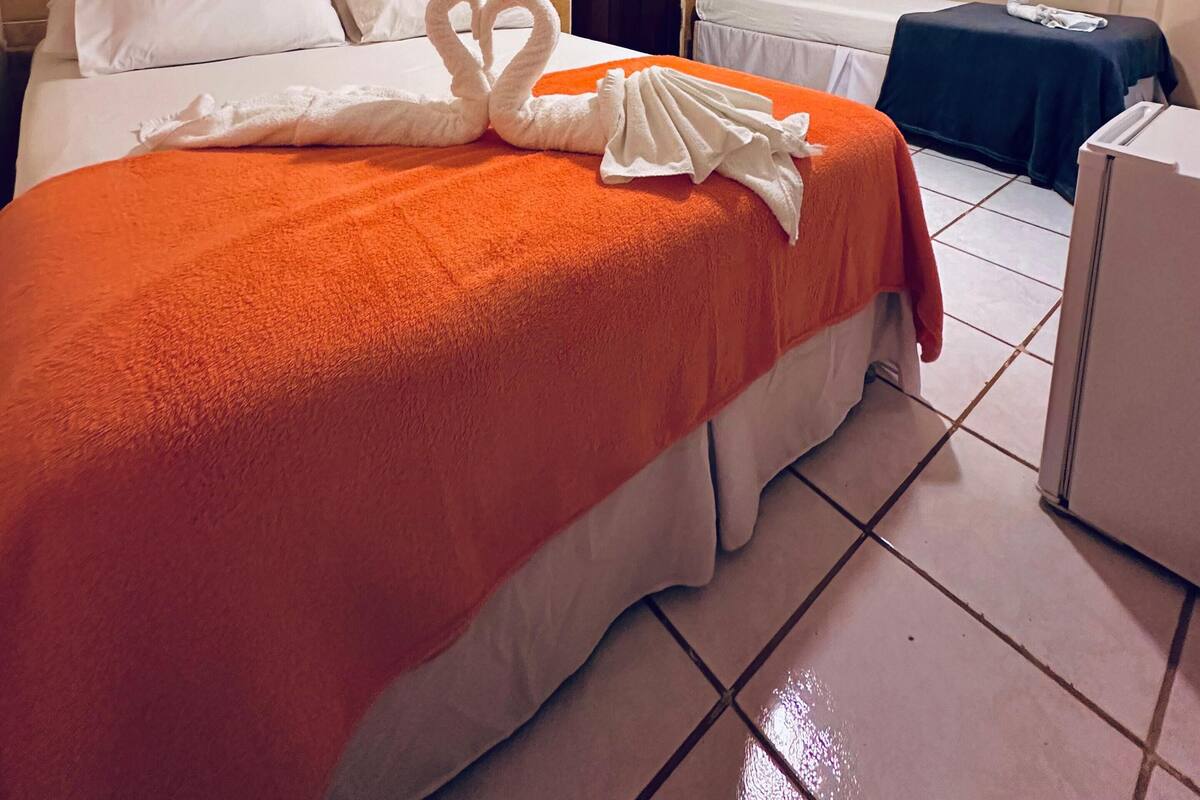 Quarto de hotel com uma cama, outra cama, uma secretária e uma porta.