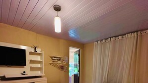 A hotel room with a bed, a TV, a desk with a chair, and a window with curtains. - Pousada Golfinho (Fernando de Noronha)
