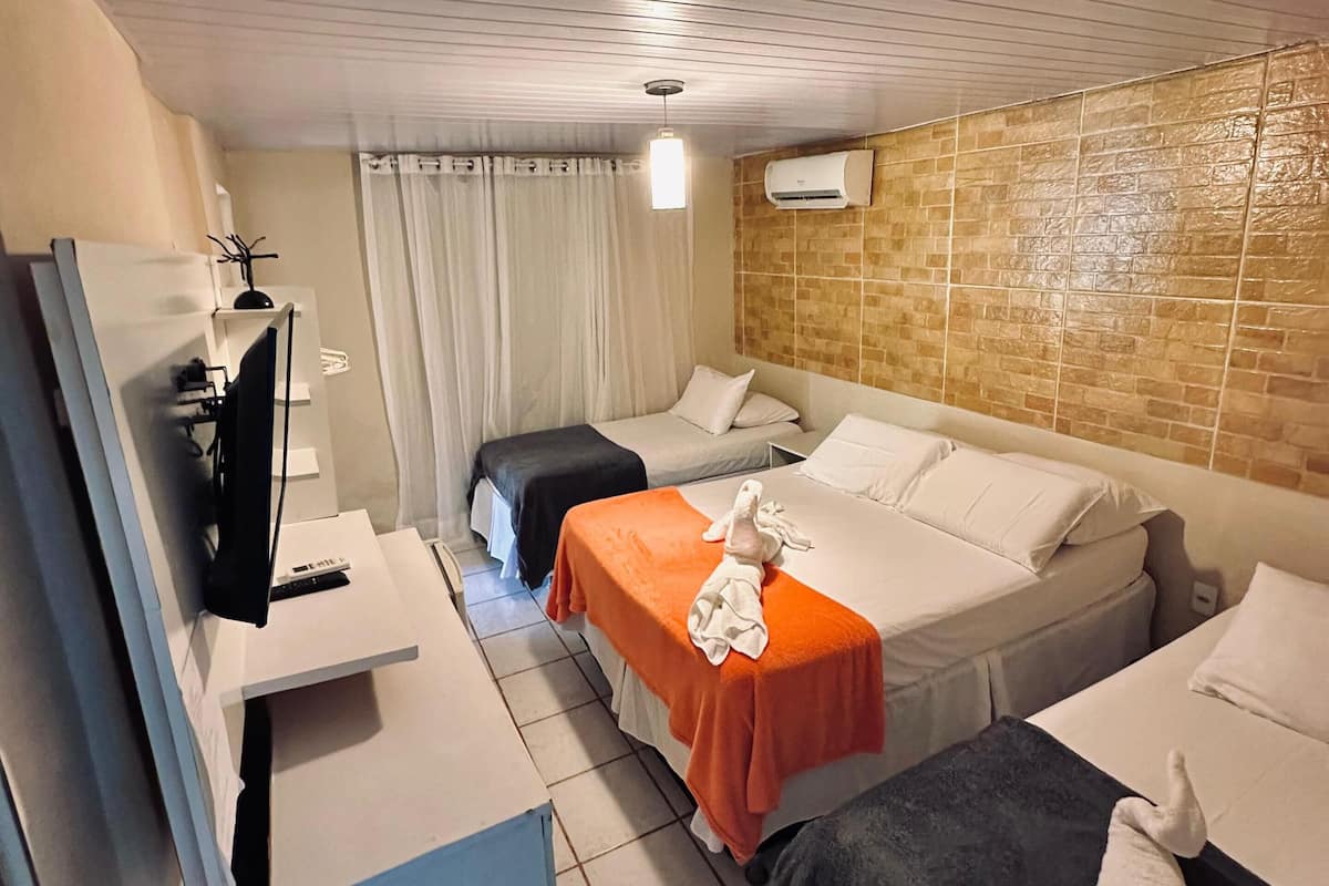 Quarto de hotel com duas camas, televisão, espelho, mesinha e ar condicionado.