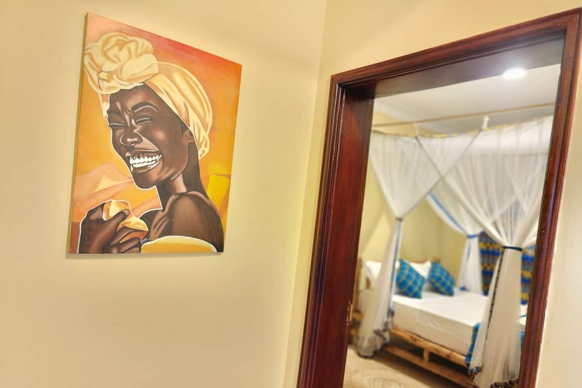 A bedroom with a bed under a canopy, a painting on the wall, and a wooden door frame.