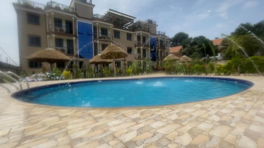 Une piscine entourée d’une terrasse dallée de pierre, de parasols à toits de chaume et d’un immeuble à plusieurs étages doté de balcons.