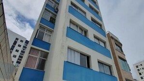 Un edificio residencial de varios pisos con fachada plana, balcones y una zona de entrada con tejas y asientos al aire libre.
