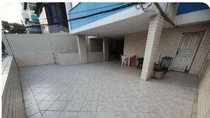 Un patio techado con piso de baldosas, un espacio de asientos con sillas de plástico y una planta en maceta.