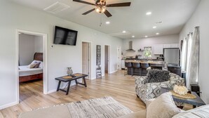A spacious living area with a sofa, a coffee table, and a TV mounted on the wall. There is a kitchen area with a dining table and chairs. - Walkable Neighborhood! Extended Stay in McAlester (McAlester)