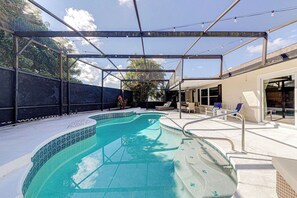 A swimming pool with a tiled edge, a covered patio area with lounge chairs, and a view of the surrounding landscape.