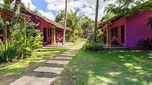 A pathway leading to a building with a thatched roof and a pink exterior. - Villa Maravilha (Porto Seguro)