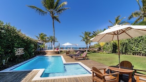 A wooden deck with a swimming pool, lounge chairs, and a table with an umbrella. - Villa Maravilha (Porto Seguro)