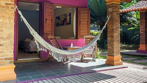 A hammock on a patio with a bed visible through an open door. - Villa Maravilha (Porto Seguro)