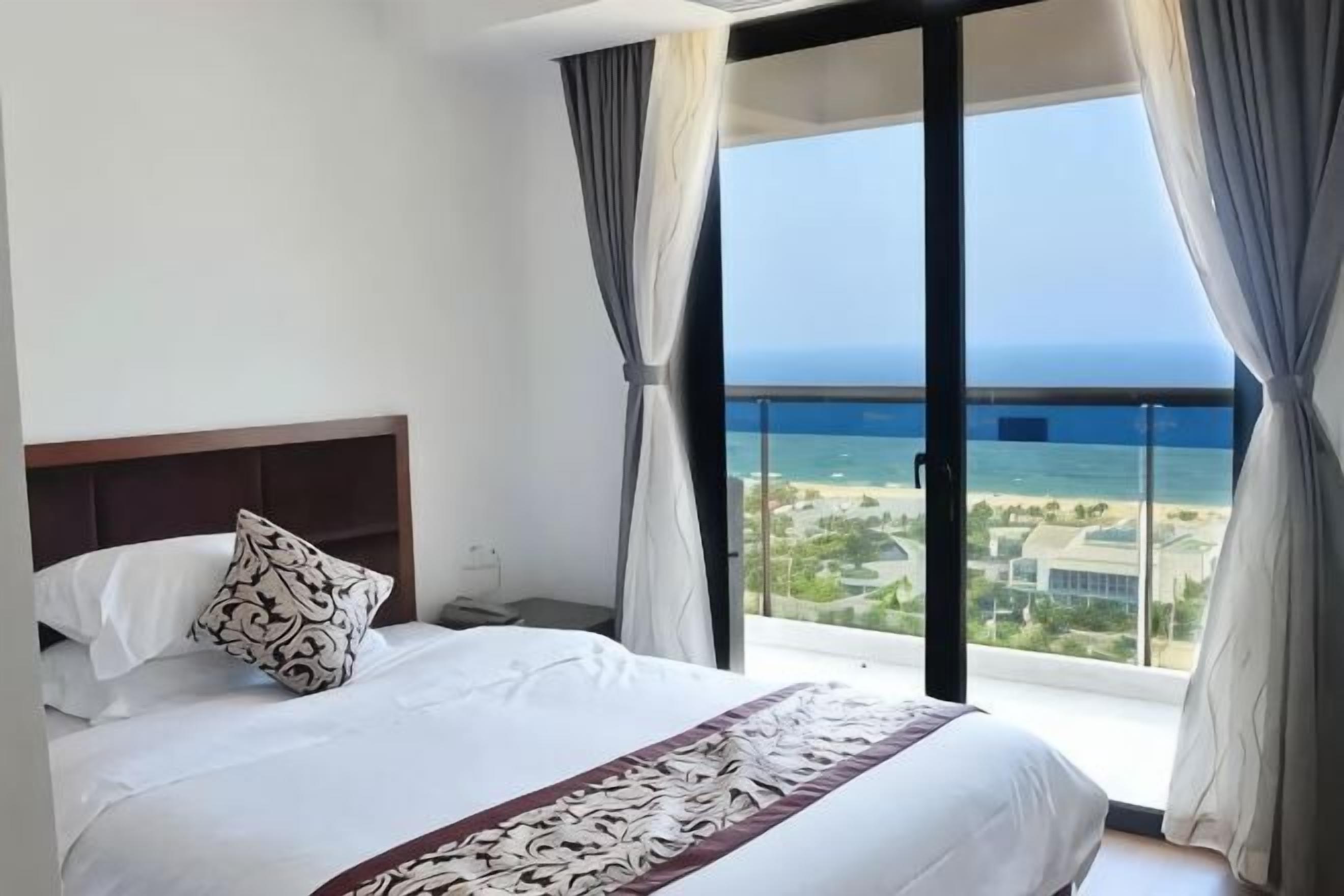 Une chambre d’hôtel avec un lit, une table de chevet, une fenêtre avec des rideaux et une vue sur l’océan.