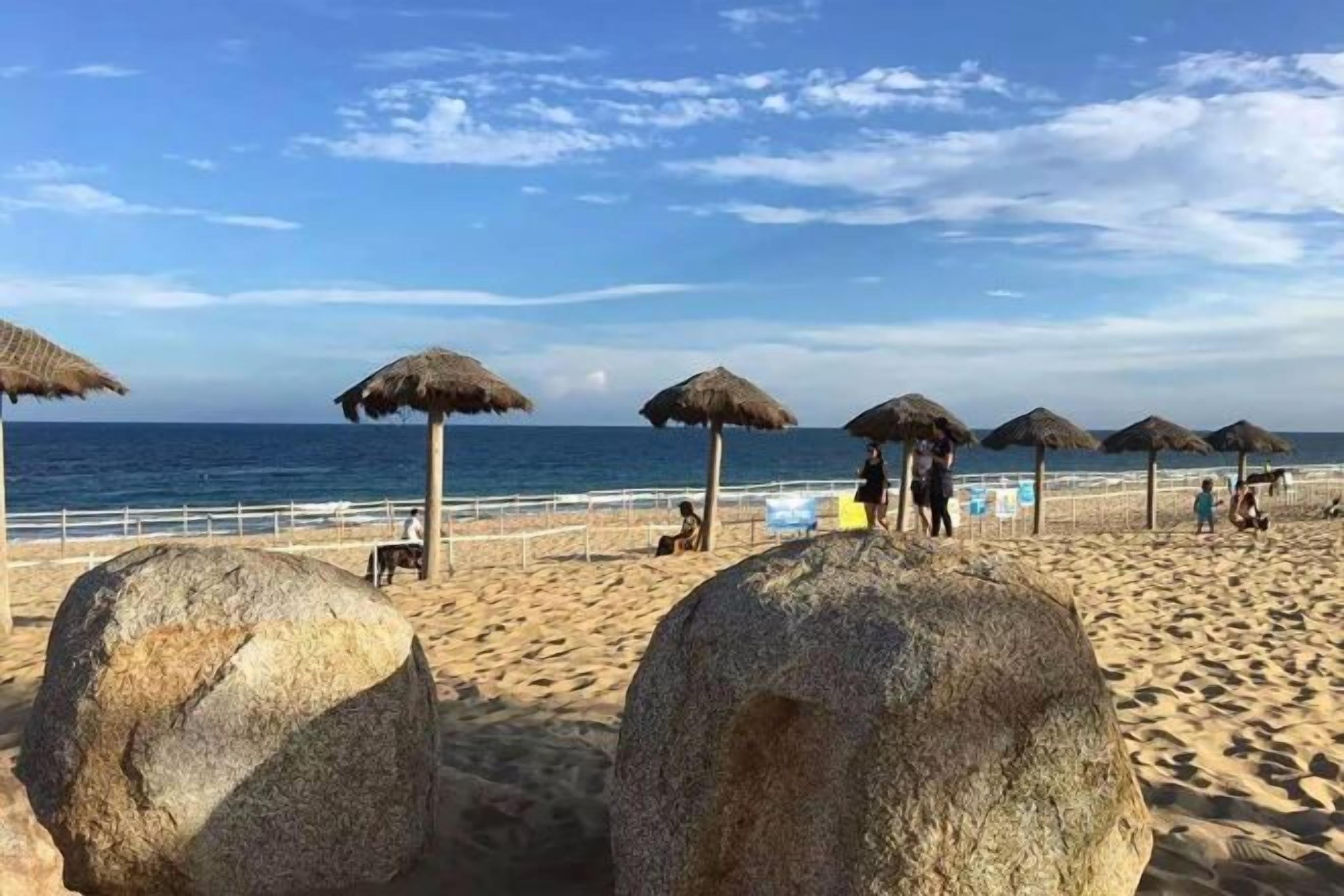 A beach with thatched umbrellas and large rocks.