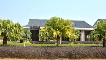 A building with a traditional tiled roof, surrounded by well-maintained hedges and palm trees.