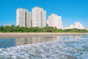 Un hotel frente a la playa con edificios altos, palmeras y una playa de arena.