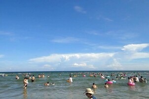 Una playa concurrida, gente en el agua y en la orilla.