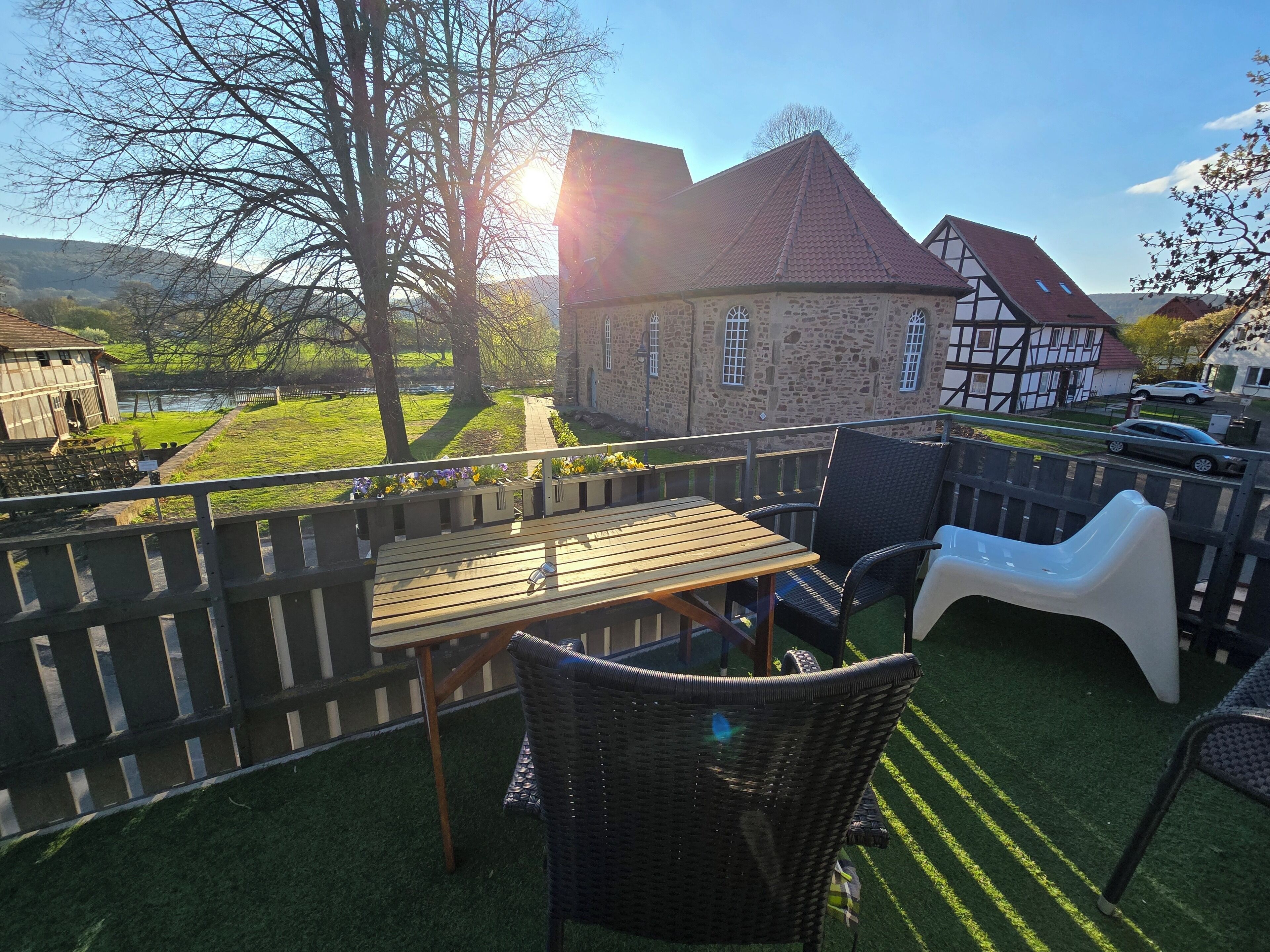 An outdoor patio with a table and chairs, a wooden fence, and a view of a traditional house.