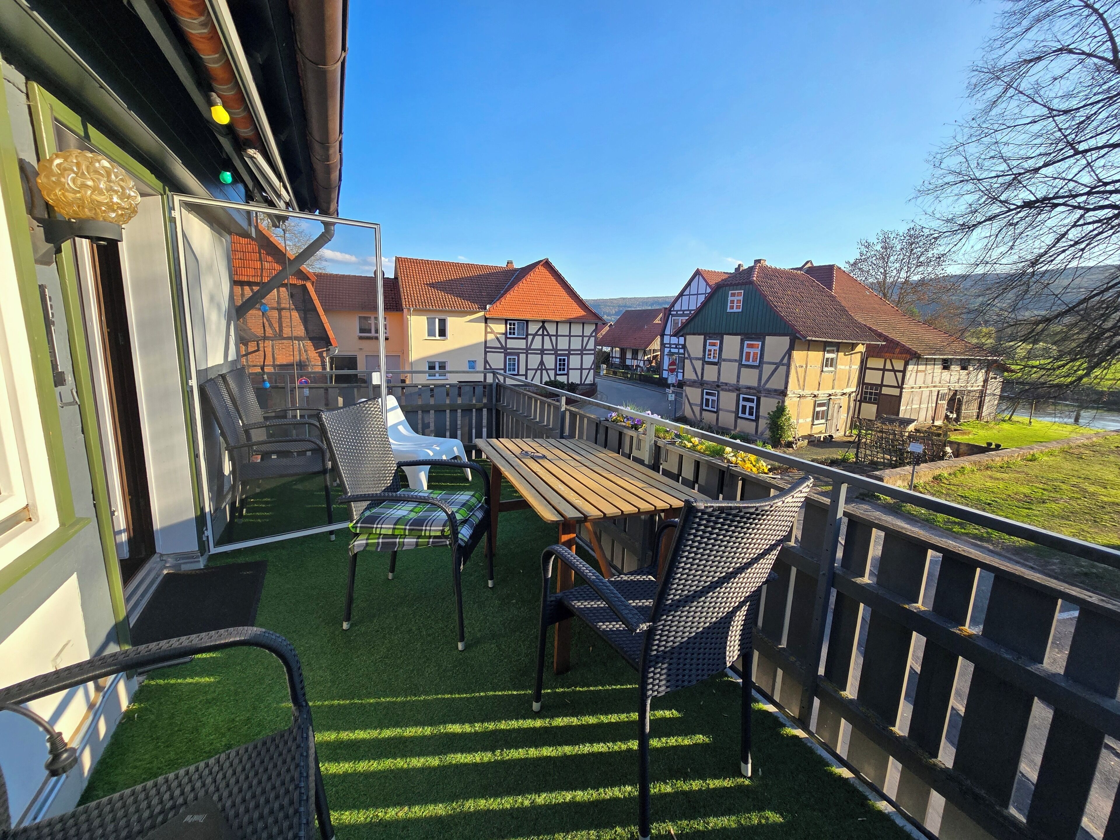 Een balkon met een houten tafel en stoelen, uitzicht op traditionele huizen en een gazon.