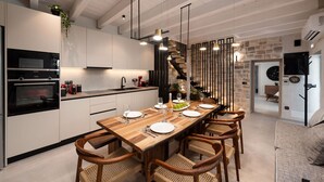 Una cuina moderna amb una taula de dinar de fusta preparada per a sis, un forn integrat i una escala que condueix a un altre pis.