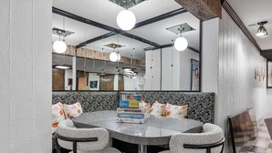 Uma sala de jantar moderna com uma mesa redonda, duas cadeiras cinzas estofadas e uma pilha de livros sobre a mesa.