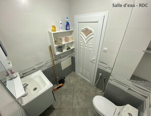 Et badeværelse med vask, toilet, brusebad og en hylde med toiletartikler.