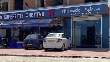 Una farmacia llamada 'Superette ChetTab' con un letrero y dos coches estacionados frente a ella.