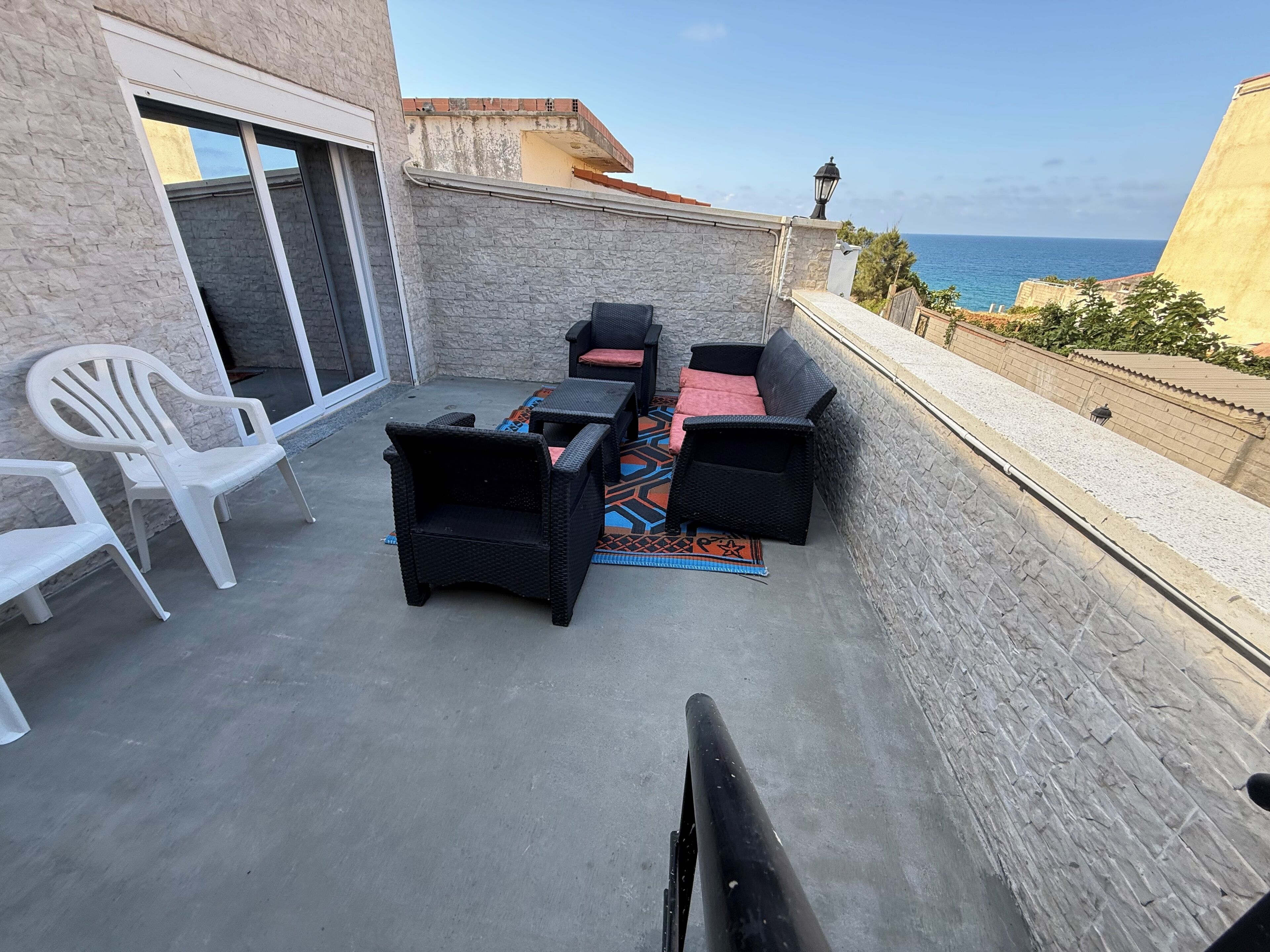 Un balcon avec des meubles d’extérieur, une vue sur la mer et un mur en pierre.