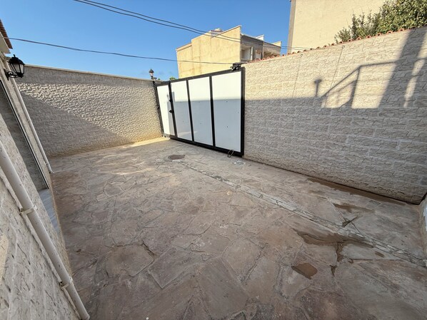 A courtyard with a stone floor, a metal gate, and a stone wall. - Maison Individuelle - Ait Chafaa Azeffoun (Aït Chafâa)