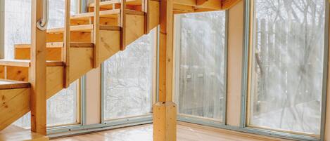 Una escalera de madera con barandas de vidrio en una habitación amplia con ventanas grandes.