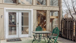 En moderne toetagers bygning med store vinduer, en overdækket terrasse med et bord og stole, og en træterrasse.