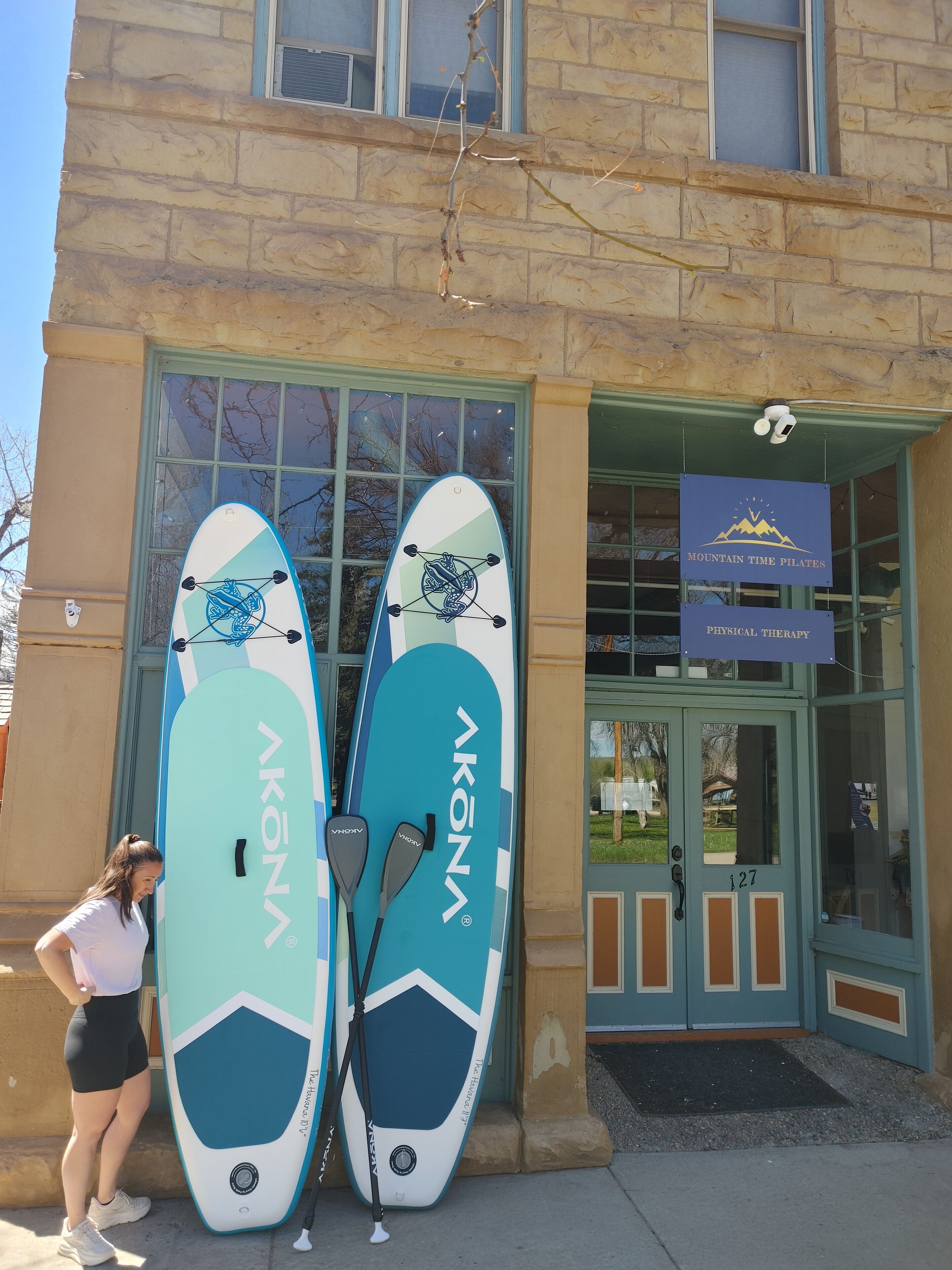 A building with a sign for Mountain Time Pilates. Two surfboards are leaning against the building.